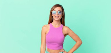 Güzel yetişkin bir kadın mutlu bir şekilde gülümsüyor, eli kalçasında ve kendinden emin.