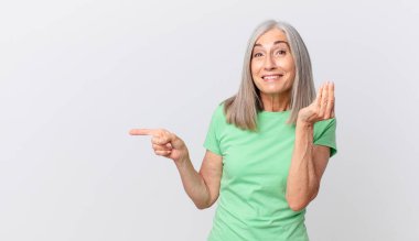 Orta yaşlı beyaz saçlı kadın kapiş ya da para hareketi yapıyor, sana ödemeni ve yan tarafı göstermeni söylüyor.