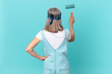 Orta yaşlı beyaz saçlı kadın duvar boyuyor.