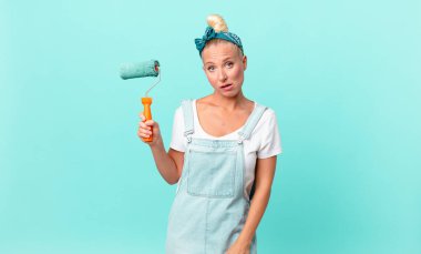 Güzel sarışın kadın şaşkın ve şaşkın hissediyor ve bir duvar boyuyor.