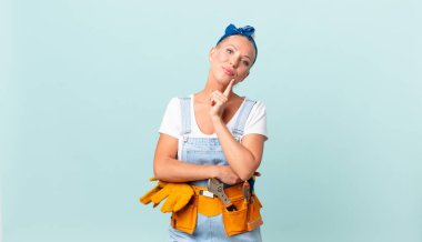 Güzel sarışın kadın mutlu bir şekilde gülümsüyor ve hayal kuruyor ya da şüphe ediyor ve ev konseptini onarıyor.