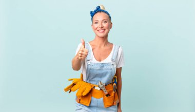 Güzel sarışın kadın gururlanıyor, olumlu gülümsüyor başparmakları havada ve ev konseptini onarıyor.