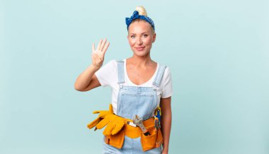 Güzel sarışın kadın gülümsüyor ve arkadaş canlısı görünüyor, dört numarayı gösteriyor ve ev konseptini onarıyor.