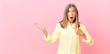 Oldukça orta yaşlı bir kadın şok olmuş ve şaşırmış görünüyor ağzı açık, kendini işaret ediyor.