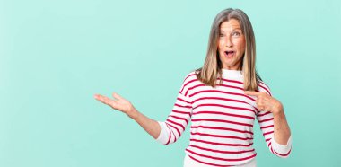 Oldukça orta yaşlı bir kadın şok olmuş ve şaşırmış görünüyor ağzı açık, kendini işaret ediyor.