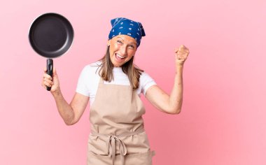 Oldukça orta yaşlı bir kadın şoke olmuş, gülüyor, başarıyı kutluyor ve elinde bir tava tutuyor. Şef konsepti