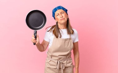 Oldukça orta yaşlı bir kadın üzgün ve mızmız görünüyor. Mutsuz görünüyor, ağlıyor ve elinde bir tava tutuyor. Şef konsepti