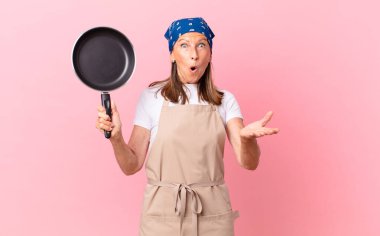 Oldukça orta yaşlı bir kadın inanılmaz bir sürprizle şaşkın ve şaşkın bir şekilde elinde bir tava tutuyor. Şef konsepti