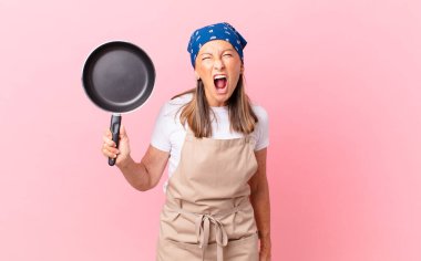 Oldukça orta yaşlı bir kadın agresif bir şekilde bağırıyor, kızgın görünüyor ve elinde bir tava tutuyor. Şef konsepti