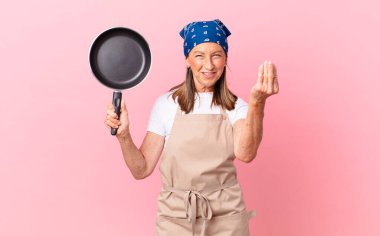 Güzel orta yaşlı bir kadın kapiş ya da para hareketi yapıyor, sana ödeme yapmanı ve elinde bir tava tutmanı söylüyor. Şef konsepti