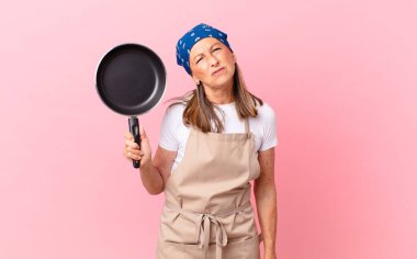 Kafası karışmış, kafası karışmış ve elinde bir tava tutan orta yaşlı bir kadın. Şef konsepti