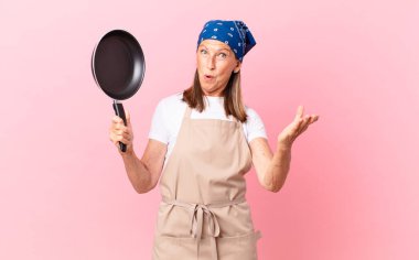 Oldukça orta yaşlı bir kadın şok olmuş, şaşırmış ve elinde bir tava tutuyor. Şef konsepti