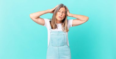 Oldukça orta yaşlı bir kadın stresli, endişeli ya da korkmuş, elleri başının üstünde.