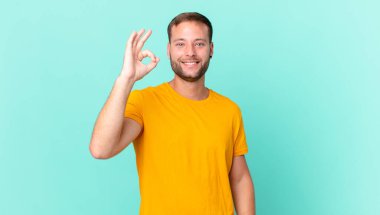 handsome blonde man feeling happy, showing approval with okay gesture
