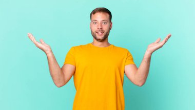 handsome blonde man feeling happy and astonished at something unbelievable