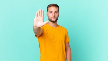 handsome blonde man looking serious showing open palm making stop gesture