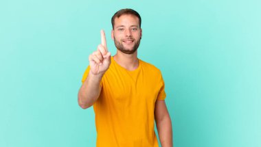 handsome blonde man smiling and looking friendly, showing number one