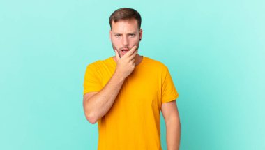 handsome blonde man with mouth and eyes wide open and hand on chin