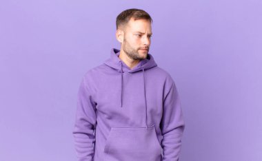 handsome blonde man feeling sad, upset or angry and looking to the side