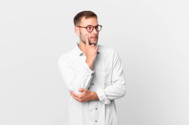 handsome blonde man smiling happily and daydreaming or doubting