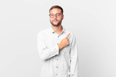 handsome blonde man smiling cheerfully, feeling happy and pointing to the side