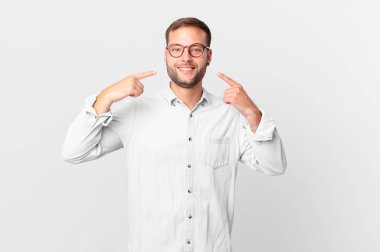 handsome blonde man smiling confidently pointing to own broad smile