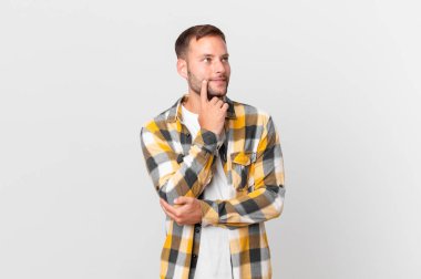 handsome blonde man smiling happily and daydreaming or doubting