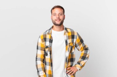 handsome blonde man smiling happily with a hand on hip and confident