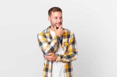 handsome blonde man smiling with a happy, confident expression with hand on chin