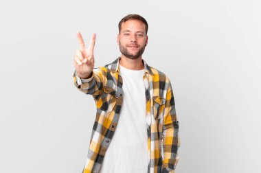 handsome blonde man smiling and looking happy, gesturing victory or peace
