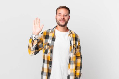 handsome blonde man smiling happily, waving hand, welcoming and greeting you