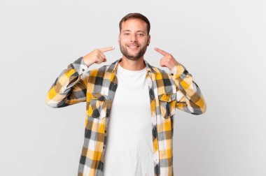 handsome blonde man smiling confidently pointing to own broad smile