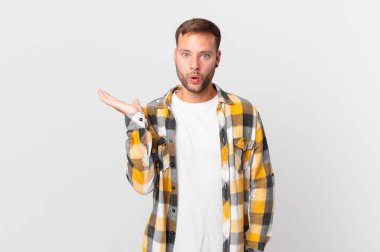 handsome blonde man looking surprised and shocked, with jaw dropped holding an object