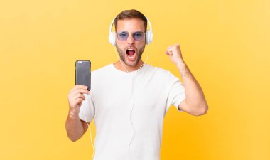 shouting aggressively with an angry expression, listening music with headphones and a smartphone