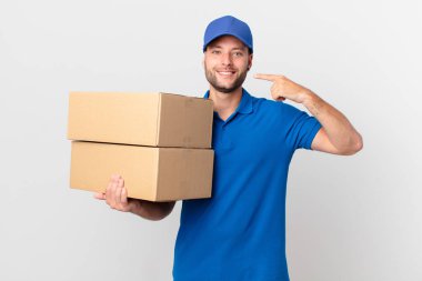 Paket teslimatçısı gülümseyerek kendi gülümsemesini işaret ediyor.