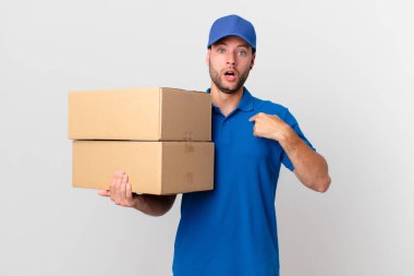 Paket teslimatçısı şok olmuş ve ağzı açık, kendini işaret ederek şaşırmış görünüyor.