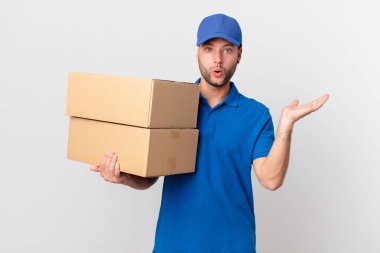 Paket teslimatçısı şaşırmış ve şok olmuş görünüyor, çenesi düşmüş bir nesne tutuyor.