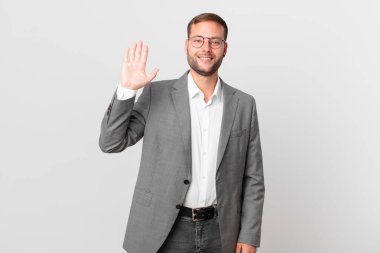 handsome businessman smiling happily, waving hand, welcoming and greeting you