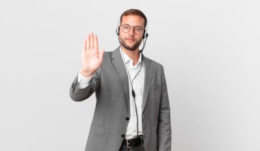 telemarketer businessman looking serious showing open palm making stop gesture