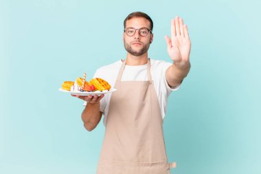Genç ve yakışıklı sarışın adam ciddi görünüyor. Avuç içini gösteriyor. Durdurma hareketi yapıyor. Waffle pişirme kavramı