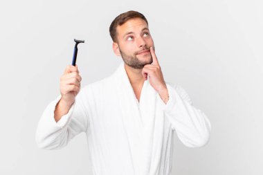 Yakışıklı sarışın adam mutlu bir şekilde gülümsüyor ve hayal kuruyor ya da şüphe ediyor. traş konsepti