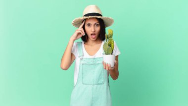 Güzel çiftçi kadın şaşırmış görünüyor, yeni bir düşünce, fikir ya da konsept fark ediyor ve elinde bir kaktüs tutuyor.