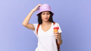 Kafası karışmış, kafası karışmış, kaşınan ve elinde dondurma tutan İspanyol bir turist.