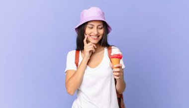 Güzel İspanyol turist mutlu, kendinden emin bir ifadeyle gülümsüyor. Elleri çenesinde ve dondurma tutuyor.