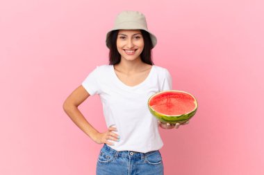 Mutlu bir şekilde gülümsüyor, eli kalçasında ve kendinden emin.