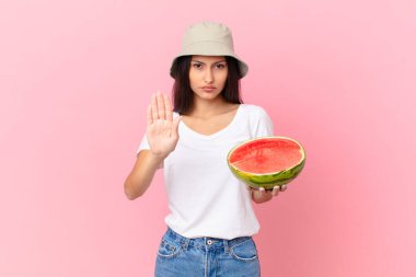 Ciddi görünüyor. Avuç içini gösteriyor. Dur hareketi yapıyor.