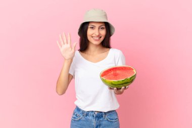 Gülümsüyor ve dost canlısı görünüyor, beş numarayı gösteriyor.