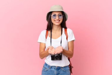 pretty hispanic tourist smiling happily with friendly and  offering and showing a concept with a photo camera and a hat