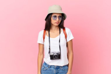 pretty hispanic tourist feeling sad, upset or angry and looking to the side with a photo camera and a hat