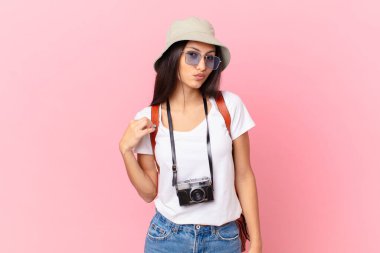 pretty hispanic tourist looking arrogant, successful, positive and proud with a photo camera and a hat